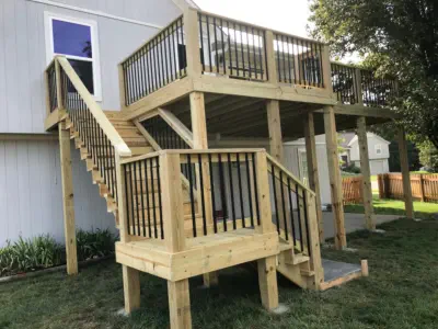 Custom pressure-treated wood deck with black aluminum balusters built by Pro Deck & Design in Kansas City, featuring multi-level staircase design with landing and expert construction for safe access to elevated outdoor living spaces in Leavenworth County