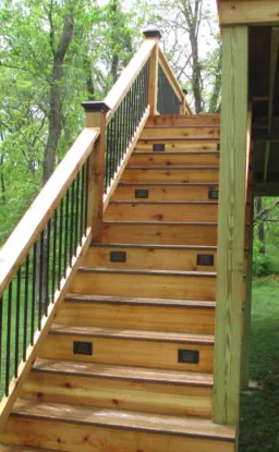 Custom cedar deck staircase with integrated step lighting built by Pro Deck & Design in Kansas City, featuring black metal balusters, premium wood construction, and professional installation for safe access in wooded Leavenworth County properties