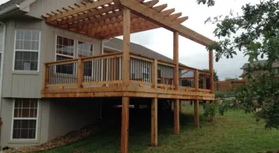 Custom elevated cedar deck with attached pergola built by Pro Deck & Design in Kansas City, featuring black metal balusters, quality craftsmanship, and perfect design solution for sloped yards in Wyandotte County neighborhoods