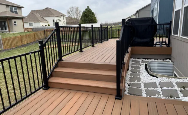 Modern composite deck with black aluminum railings installed by Pro Deck & Design in Kansas City, featuring integrated stairs, decorative stone border, and custom grilling station perfect for outdoor entertaining in new Wyandotte County subdivisions