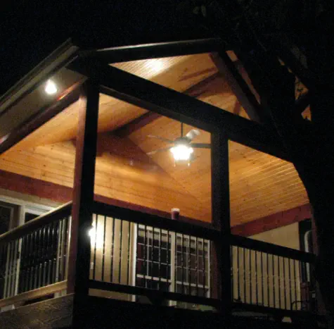 Custom covered deck in Johnson County Kansas with cedar ceiling and professional lighting installation, featuring quality nighttime outdoor living design by expert Kansas contractors specializing in all-season entertainment spaces