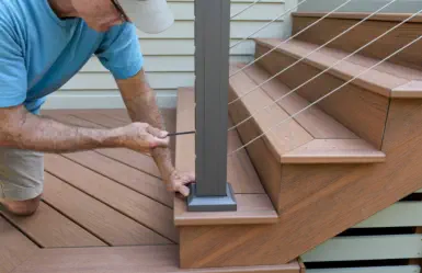 Professional deck repair and installation by Pro Deck & Design craftsman in Kansas City, showing precision drilling technique on composite deck stairs during quality renovation service in Johnson County